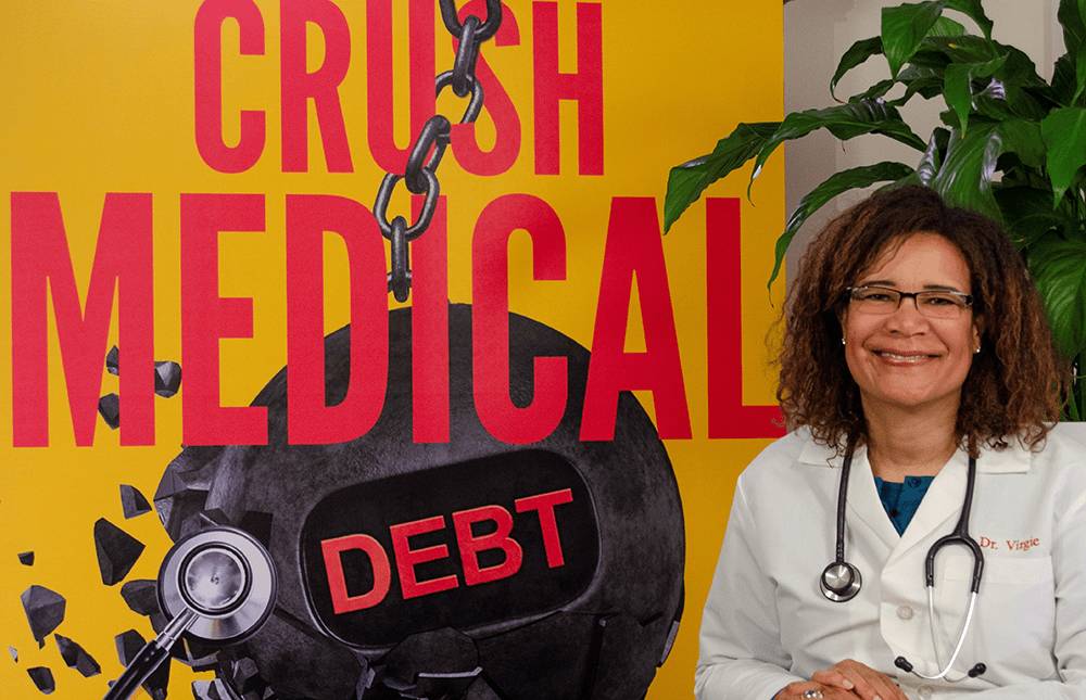 Dr. Virgie smiling in front of her Crush Medical Debt book cover