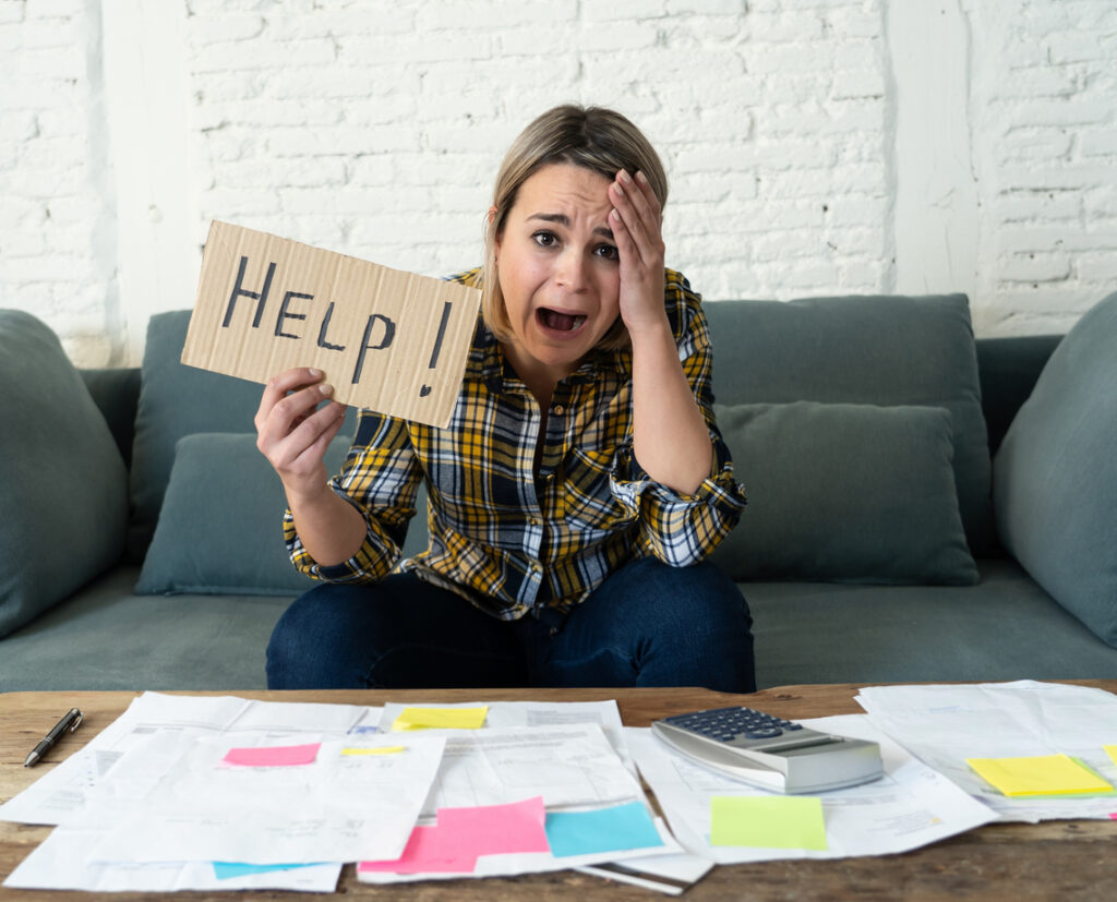 woman holding up help sign in front of a pile of medical bills